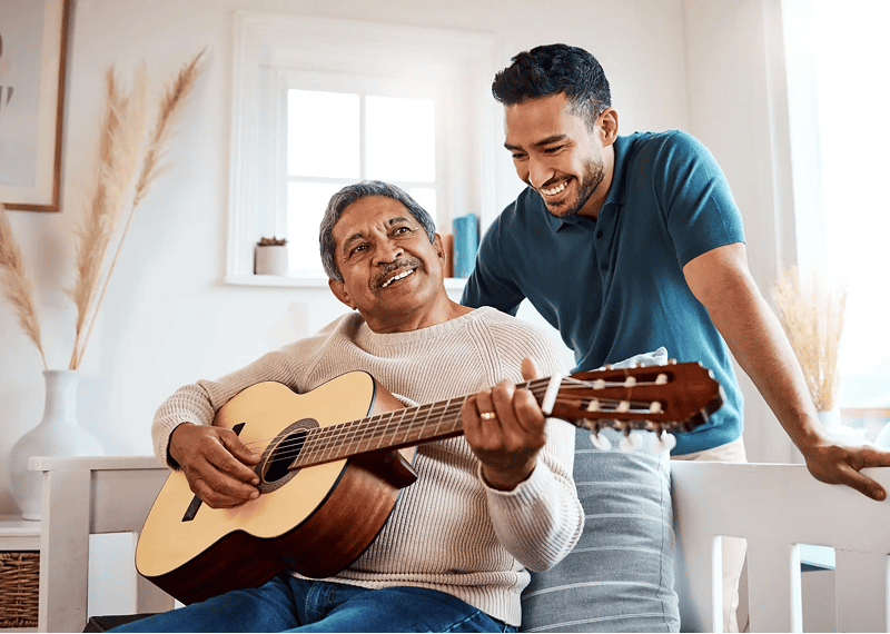 Older man playing guitar, younger man smiling