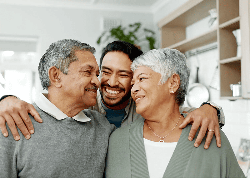 Son embracing smiling elderly parents at home